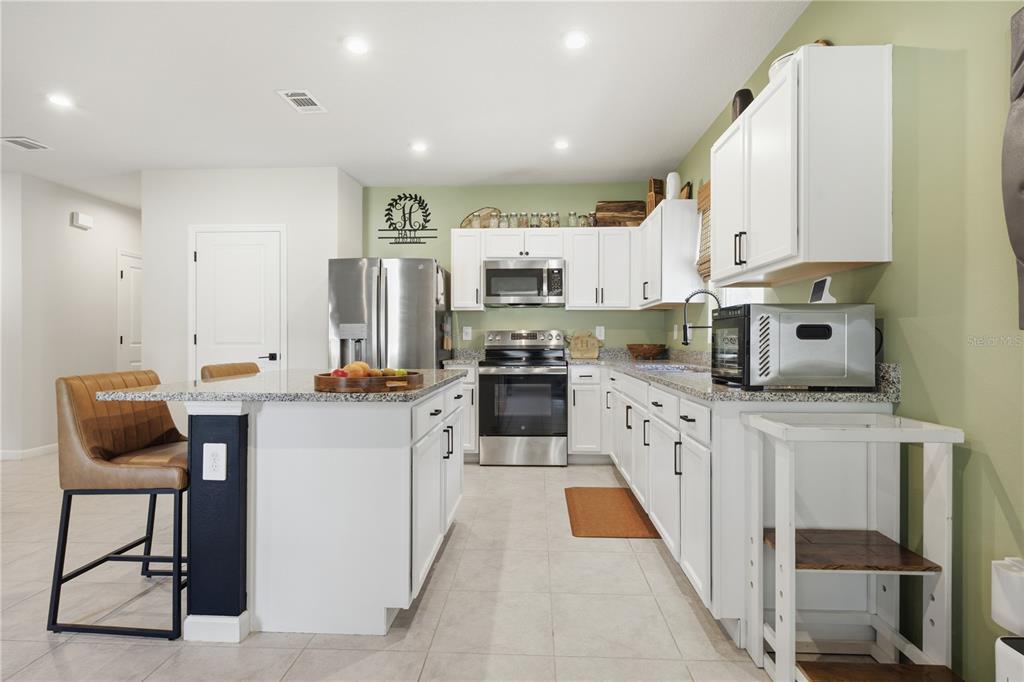A kitchen features white cabinets, granite countertops, stainless steel appliances, and a central island — 822 170TH COURT E, BRADENTON, FL