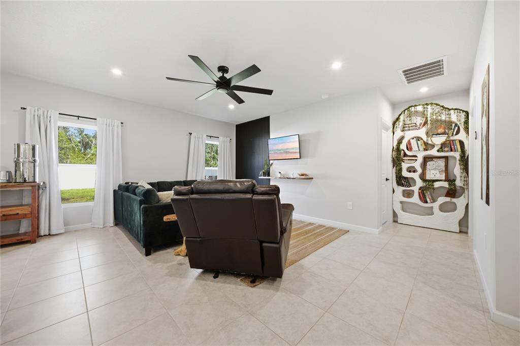 A living room features a dark sofa, a brown recliner, and a unique organic-shaped bookshelf — 822 170TH COURT E, BRADENTON, FL