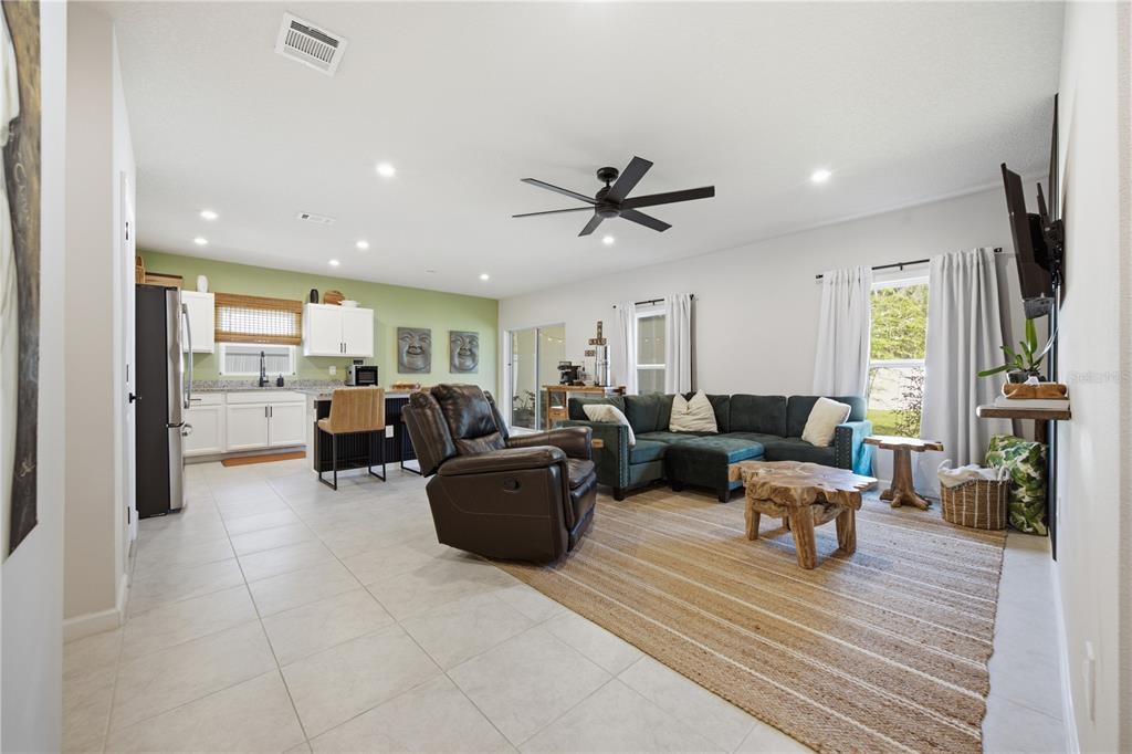 An open-concept living room and kitchen area features tile flooring, a sectional sofa, and cabinets — 822 170TH COURT E, BRADENTON, FL
