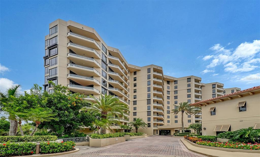 A multi-story beige apartment building features curved balconies and a paved driveway entrance — 1241 GULF OF MEXICO DRIVE UNIT 303, LONGBOAT KEY, FL