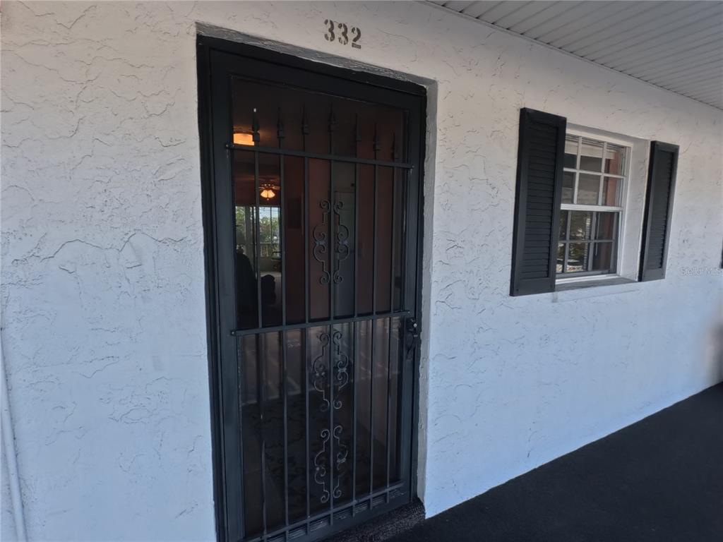 A white stucco exterior wall features a black security screen door and a window with black shutters — 202 47TH AVENUE DRIVE W UNIT 332, BRADENTON, FL