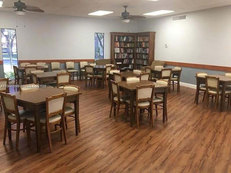 A community room features multiple dining tables, chairs, bookshelves, and wood-look flooring — 200 Berkley Rd # 123, Hollywood FL 33024, HOLLYWOOD, FL