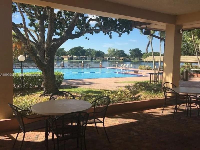 A covered patio with outdoor tables overlooks a swimming pool and a lake — 200 Berkley Rd # 123, Hollywood FL 33024, HOLLYWOOD, FL