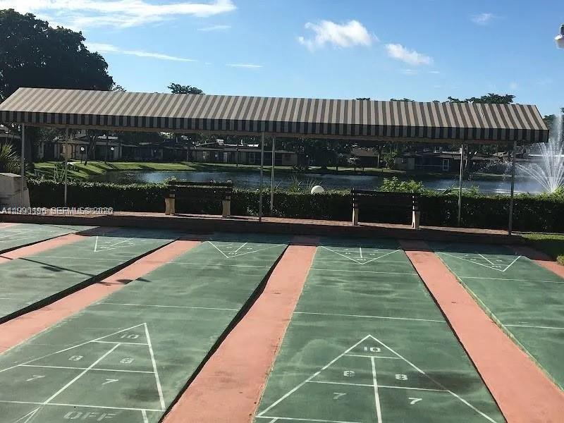 An outdoor shuffleboard court sits under a striped awning beside a pond — 200 Berkley Rd # 123, Hollywood FL 33024, HOLLYWOOD, FL