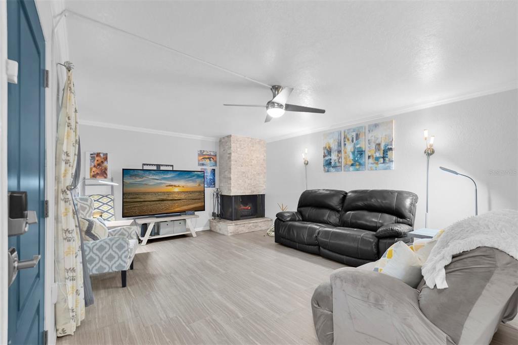 A living room features a stone fireplace, a ceiling fan, and light wood-look flooring — 9476 TRADEWINDS AVENUE UNIT 9476, SEMINOLE, FL