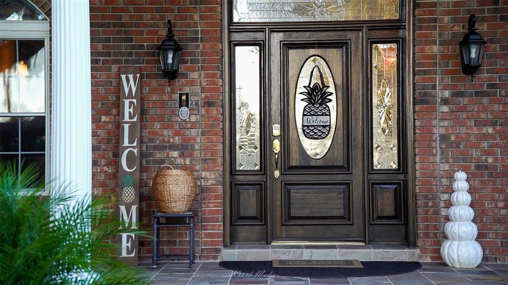 A brick house entrance features a wooden door with a pineapple accent and welcome sign — 150 LAKE WINNEMISSETT DRIVE, DELAND, FL