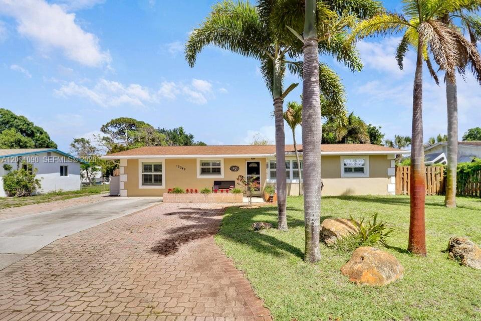 A single-story house with a tan exterior, a brick driveway, and palm trees in the yard — 19049 SE Robert Drive, Jupiter FL 33469, JUPITER, FL