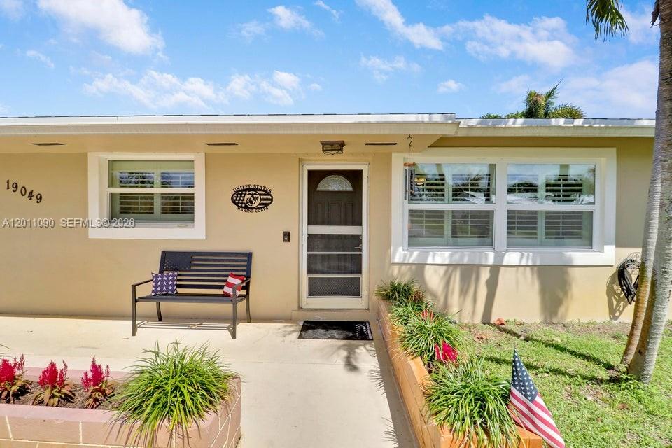 The exterior of a single-story house features a front porch, a bench, and landscaping — 19049 SE Robert Drive, Jupiter FL 33469, JUPITER, FL