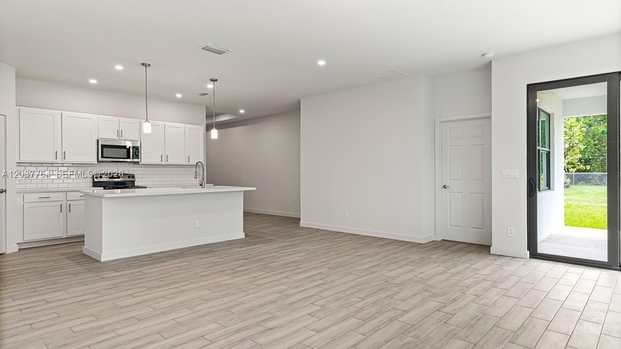 A modern kitchen with white cabinetry and an island opens into a spacious living area — 7704 Pacific Ave, Fort Pierce FL 34951, FORT PIERCE, FL