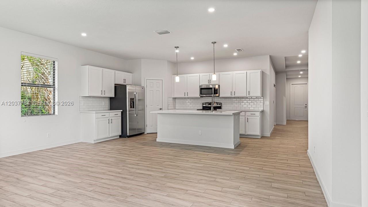 A modern kitchen features white cabinets, stainless steel appliances, an island, and light wood flooring — 7704 Pacific Ave, Fort Pierce FL 34951, FORT PIERCE, FL
