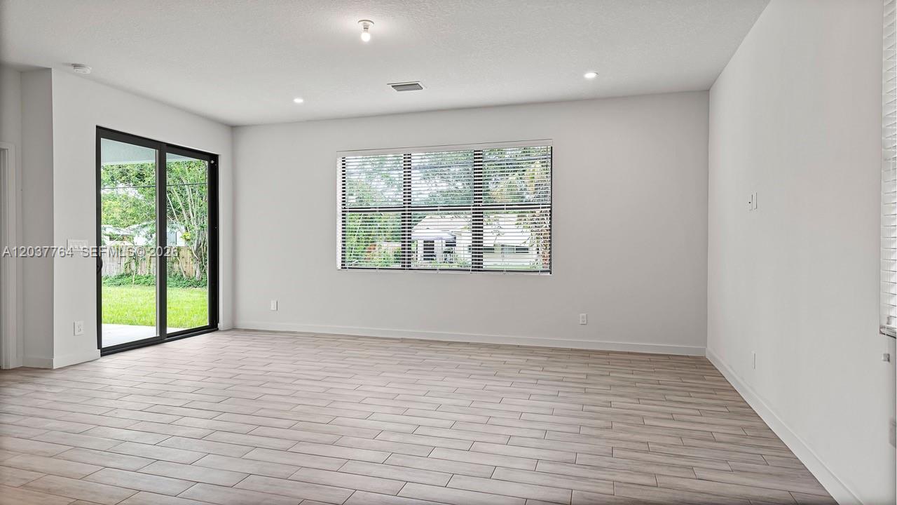 An empty room features light wood-look tile flooring, white walls, and a sliding glass door — 7704 Pacific Ave, Fort Pierce FL 34951, FORT PIERCE, FL