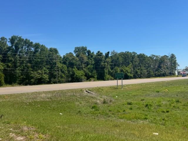 A paved road runs alongside a grassy field with a line of trees in the background — 00 SPRING HILL DRIVE, BROOKSVILLE, FL