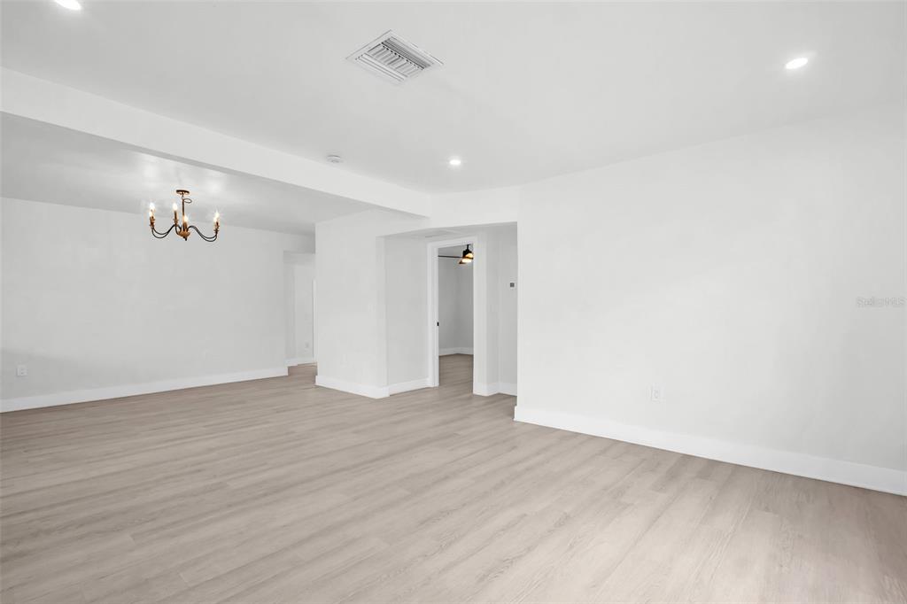 A bright, open-concept living area features light wood-look flooring, white walls, and a chandelier — 4000 GROVE STREET S, ST PETERSBURG, FL