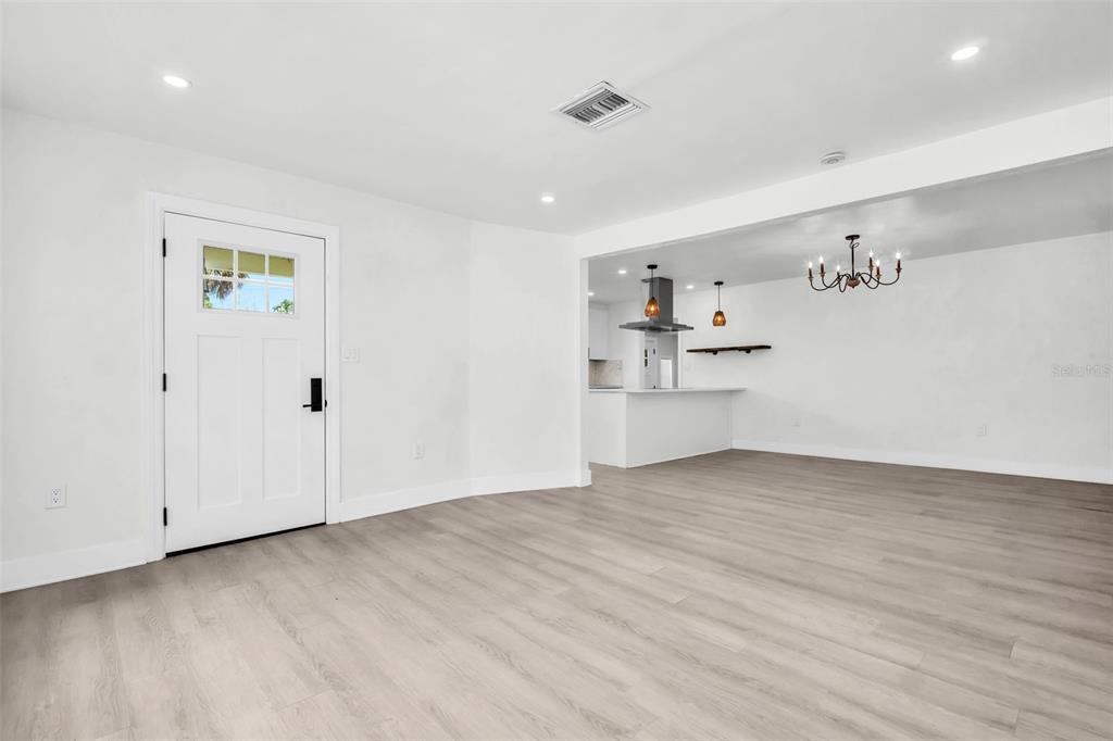 A bright, open-concept living area features light wood-look flooring, white walls, and a white door — 4000 GROVE STREET S, ST PETERSBURG, FL