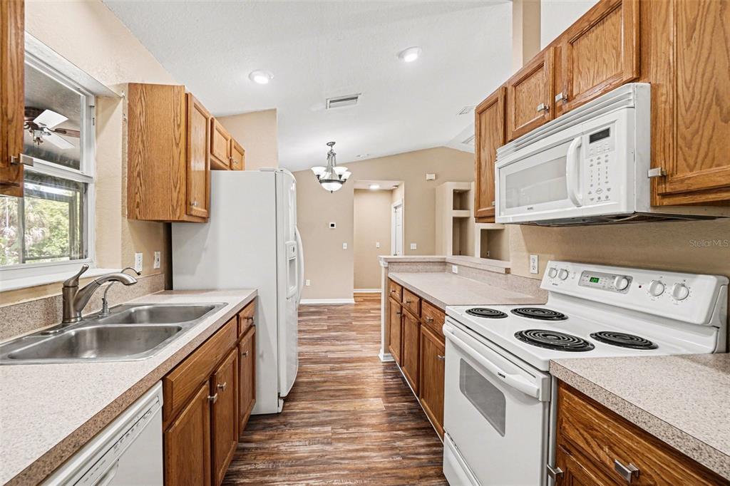 A kitchen features wood cabinets, white appliances, laminate countertops, and wood-look flooring — 4431 ANDRIS ST, NORTH PORT, FL
