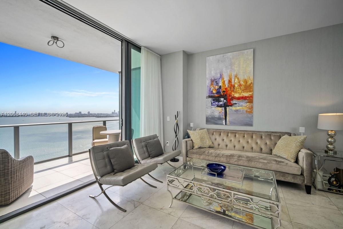 A living room features a velvet sofa, glass coffee table, and a balcony overlooking water — 480 NE 31 # 2707, Miami FL 33137, MIAMI, FL