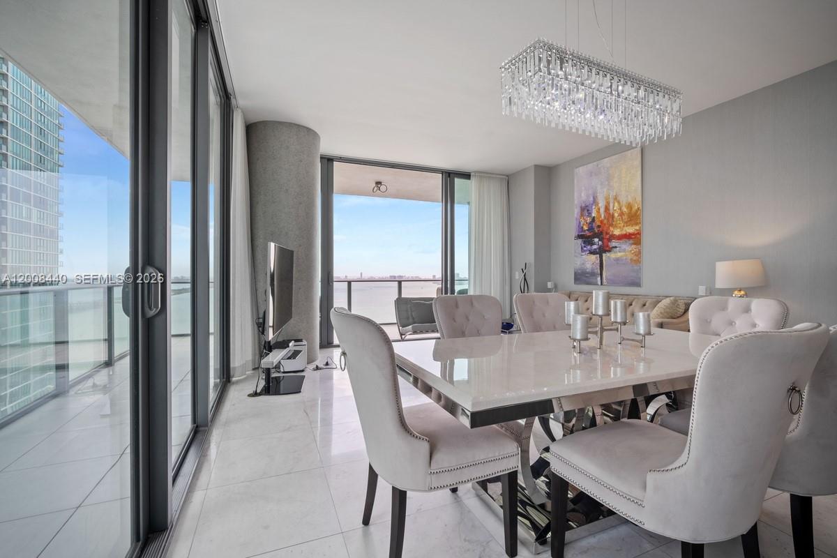 A dining room features a white table, tufted chairs, a crystal chandelier, and floor-to-ceiling windows — 480 NE 31 # 2707, Miami FL 33137, MIAMI, FL