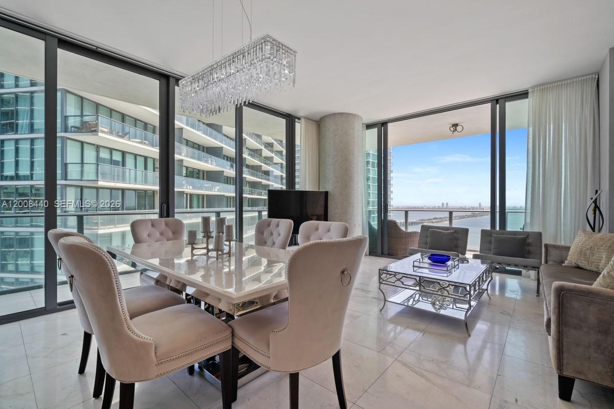 A modern dining and living area features floor-to-ceiling windows, marble floors, and a crystal chandelier — 480 NE 31 # 2707, Miami FL 33137, MIAMI, FL