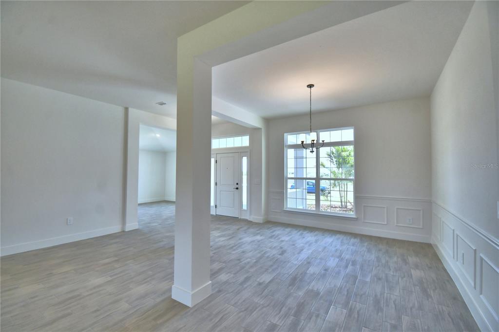 An open-concept dining room features light wood-look tile flooring, white wainscoting, and a chandelier — 5415 WATERSIDE DRIVE, AUBURNDALE, FL