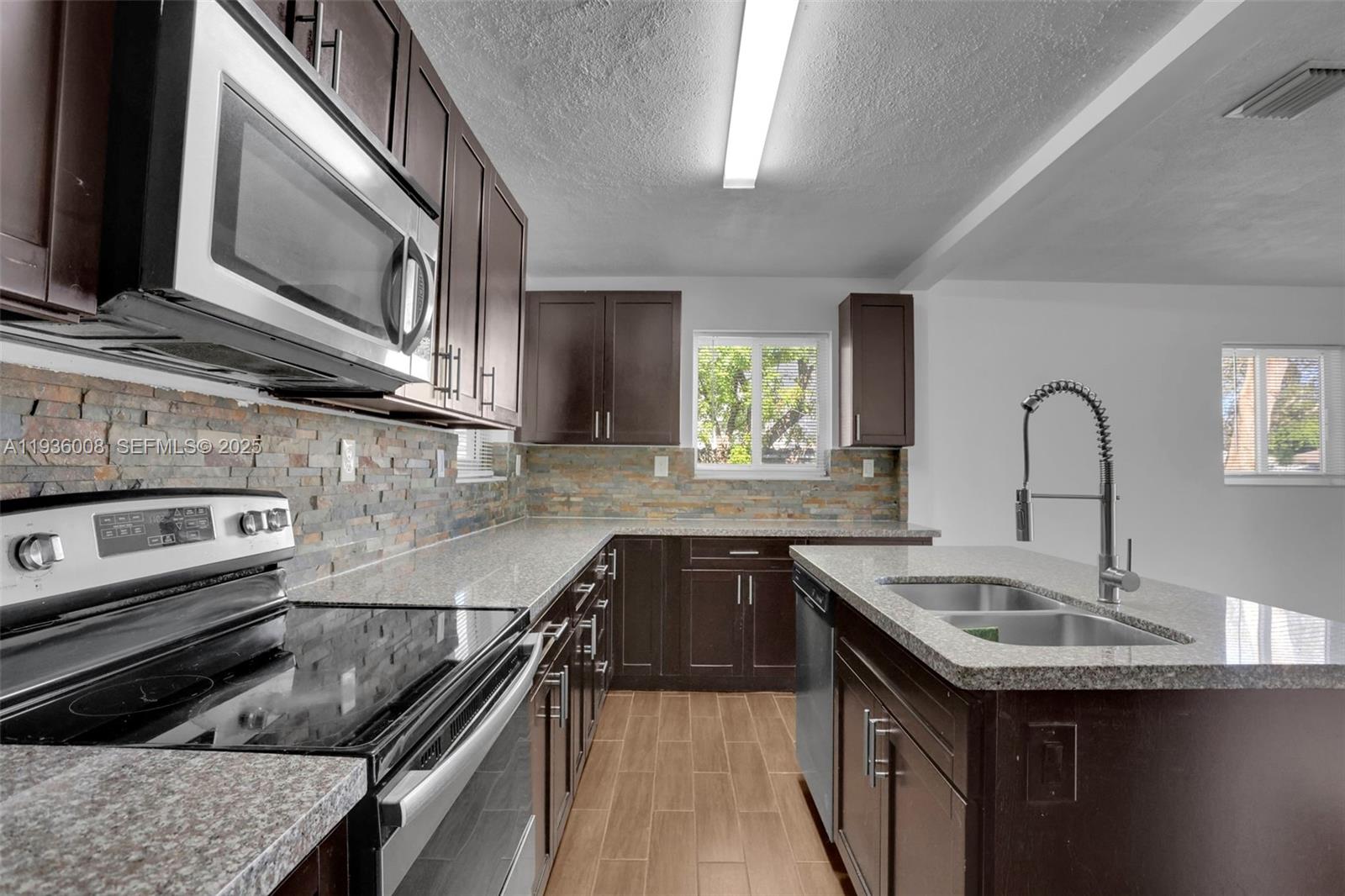 A kitchen features dark wood cabinets, granite countertops, a stone backsplash, and a center island — 510 N 69th Ave # 0, Hollywood FL 33024, HOLLYWOOD, FL