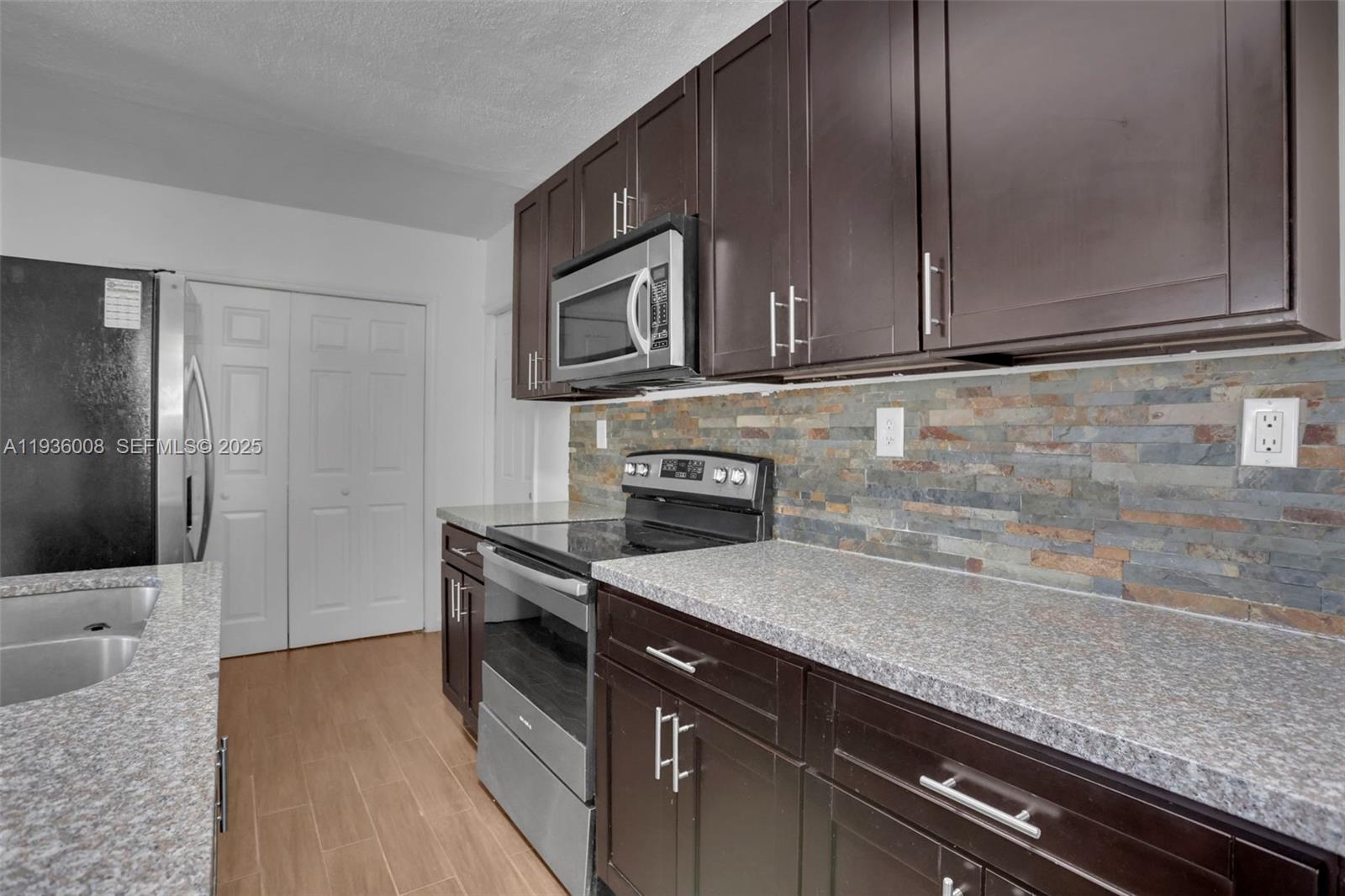 A kitchen features dark wood cabinets, granite countertops, a stone backsplash, and stainless steel appliances — 510 N 69th Ave # 0, Hollywood FL 33024, HOLLYWOOD, FL