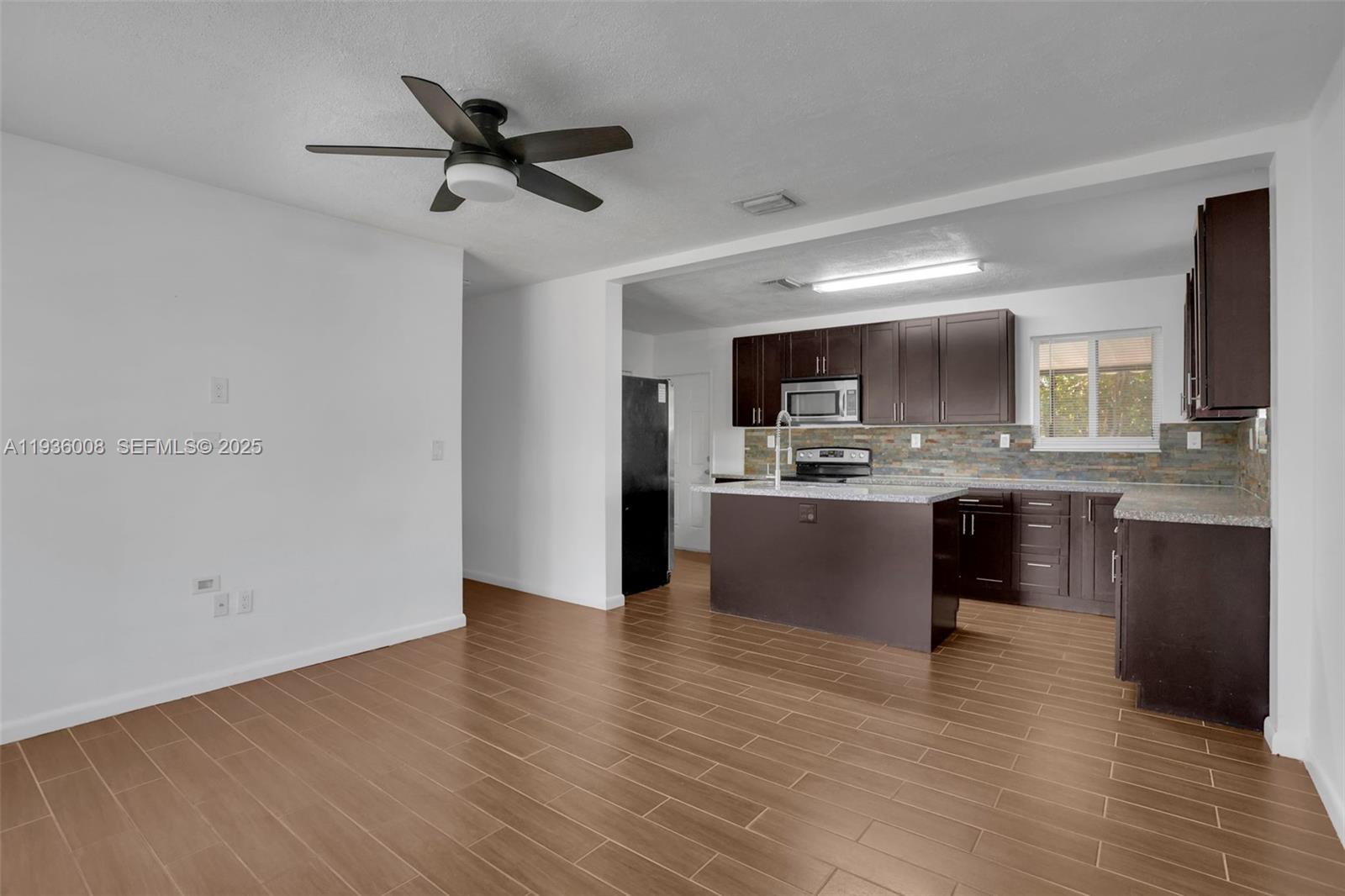 A kitchen with dark cabinets and a central island opens into a living area — 510 N 69th Ave # 0, Hollywood FL 33024, HOLLYWOOD, FL
