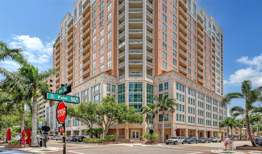 A tall, multi-story apartment building stands at a street corner with palm trees and signage — 1350 MAIN STREET UNIT 1407, SARASOTA, FL
