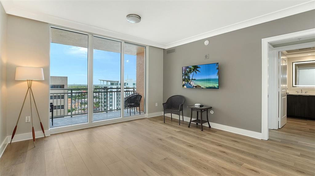 A living room with light wood flooring, a wall-mounted television, and a balcony with views — 1350 MAIN STREET UNIT 1407, SARASOTA, FL