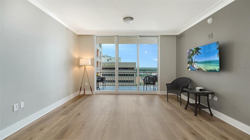 A living room features light wood flooring, a wall-mounted television, and a balcony with seating — 1350 MAIN STREET UNIT 1407, SARASOTA, FL