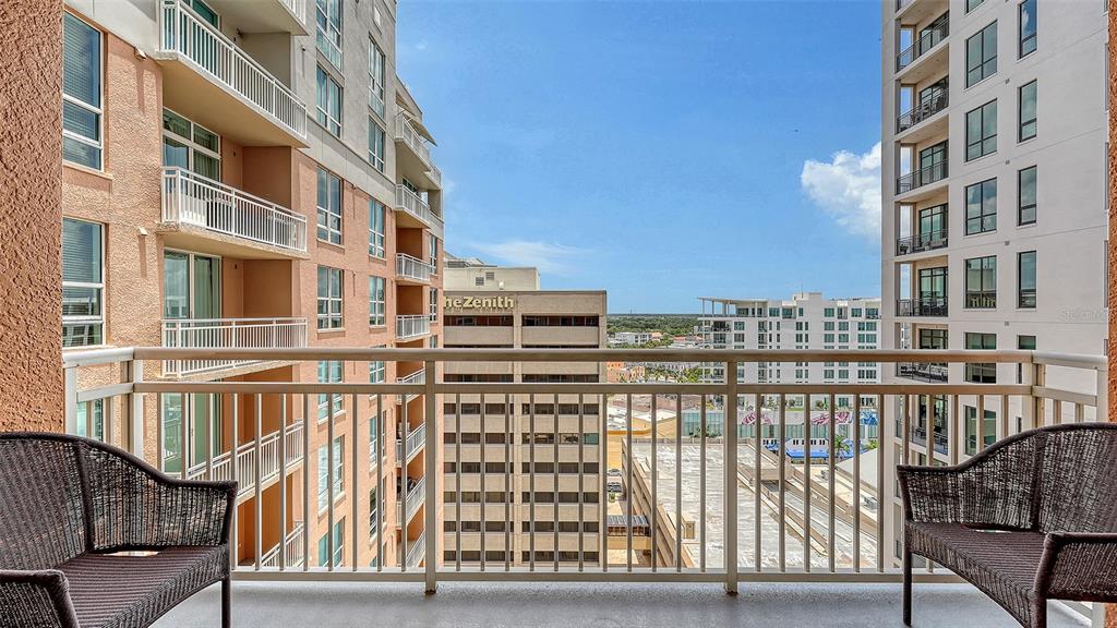 A balcony with two chairs overlooks a city street between two tall apartment buildings — 1350 MAIN STREET UNIT 1407, SARASOTA, FL