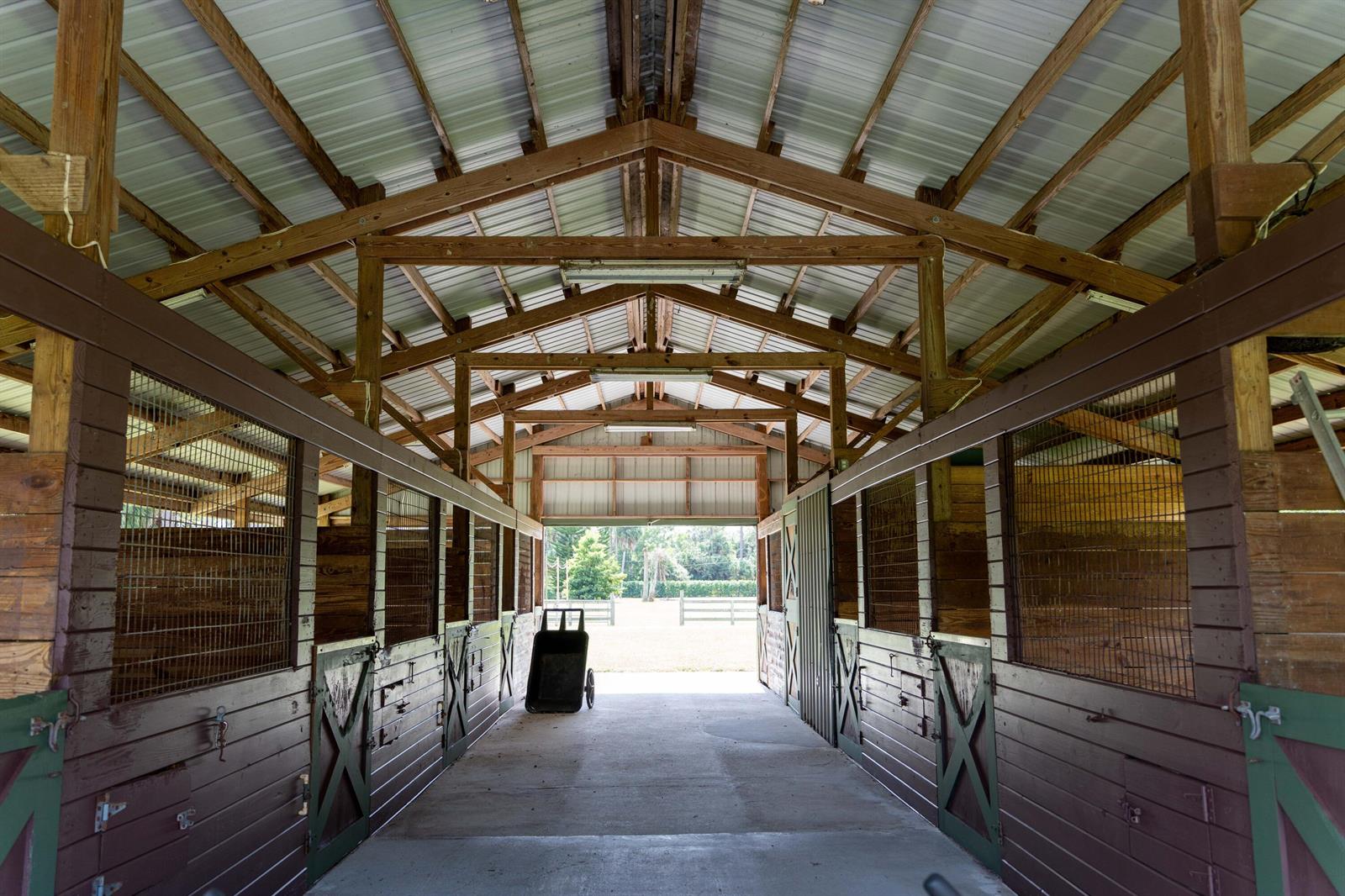 An interior view of a horse barn aisle with wooden stalls and a concrete floor — 14279 43rd Road N, FL 33470, FL