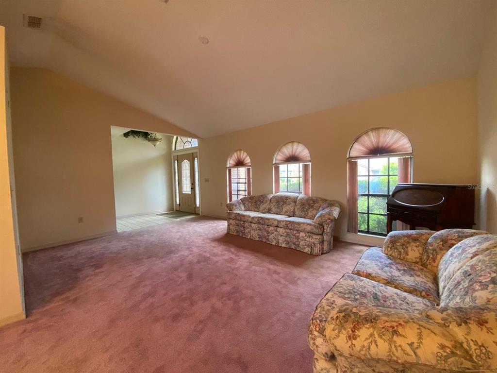 A living room features vaulted ceilings, pink carpeting, floral sofas, and three arched windows — 508 BROKENSHIRE DRIVE, DEBARY, FL