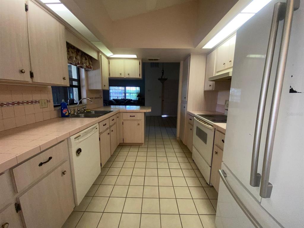 A kitchen features light-colored cabinets, tiled countertops, white appliances, and a tiled floor — 508 BROKENSHIRE DRIVE, DEBARY, FL
