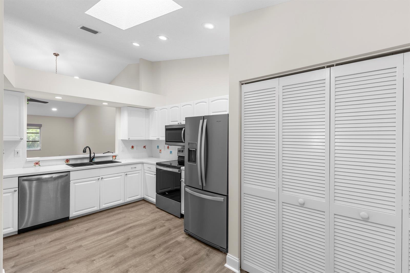 A kitchen features white cabinets, stainless steel appliances, a pass-through window, and wood-look flooring — 9760 Summerbrook Terrace # A, Boynton Beach FL 33437, BOYNTON BEACH, FL