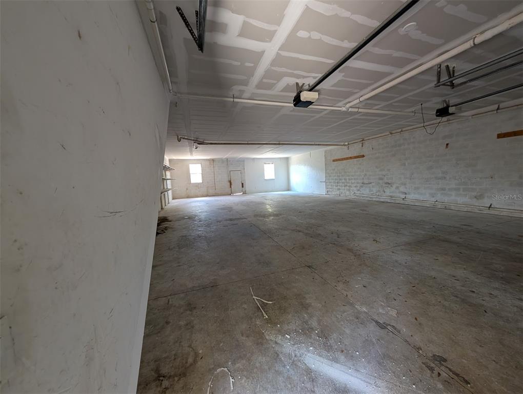 A large, unfinished garage space with concrete floors, white block walls, and exposed ceiling pipes — 3006 HAWTHORNE STREET, SARASOTA, FL