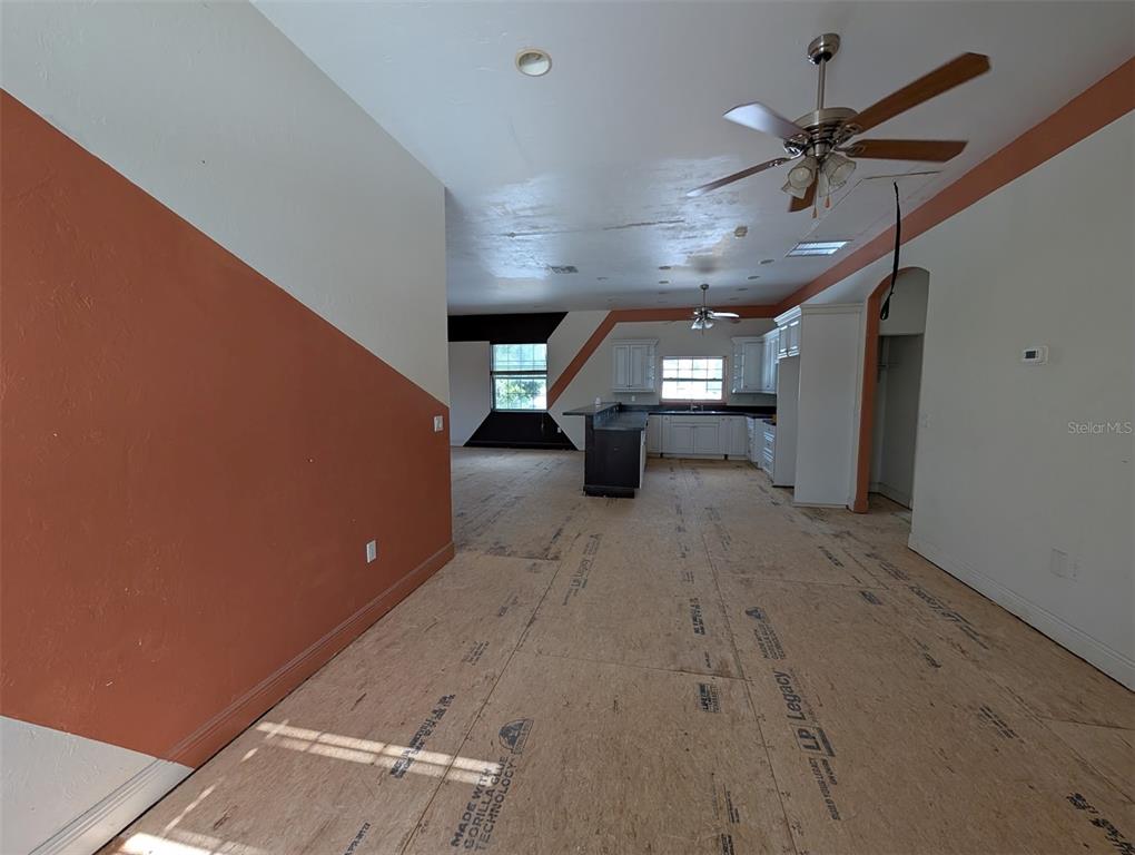 An open-concept room with unfinished subflooring, a kitchen area, and walls painted with orange accents — 3006 HAWTHORNE STREET, SARASOTA, FL