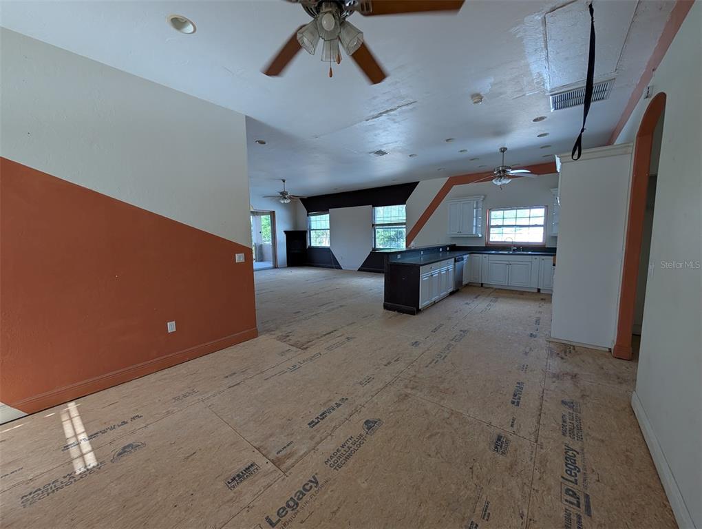 An open-concept room features unfinished subflooring, a kitchen with white cabinets, and orange accent walls — 3006 HAWTHORNE STREET, SARASOTA, FL