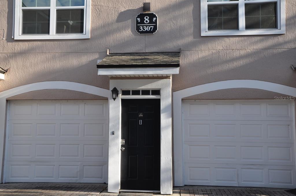 A two-story townhouse exterior features a central black front door flanked by two white garages — 3307 GREENWICH VILLAGE BOULEVARD UNIT 205, ORLANDO, FL