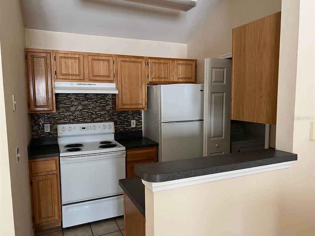 A kitchen features wood cabinets, a white stove, a refrigerator, and a tiled backsplash — 3307 GREENWICH VILLAGE BOULEVARD UNIT 205, ORLANDO, FL