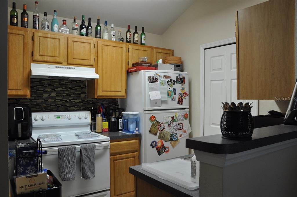 A kitchen features light wood cabinets, a white stove, a refrigerator, and bottles displayed above — 3307 GREENWICH VILLAGE BOULEVARD UNIT 205, ORLANDO, FL
