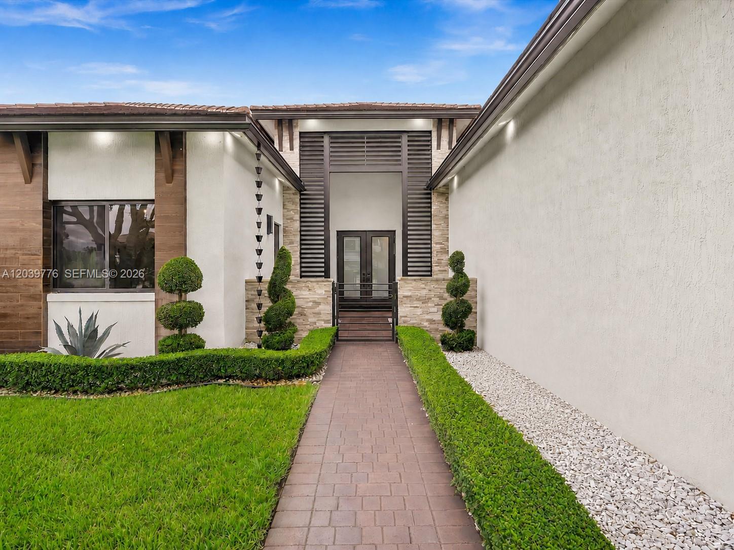 A paved walkway leads to the front entrance of a modern home with landscaped hedges — 4980 SW 159th Ave, Southwest Ranches FL 33331, SOUTHWEST RANCHES, FL