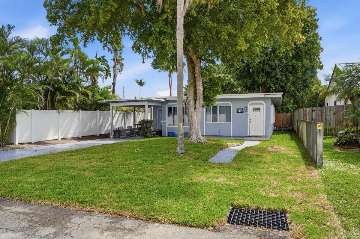 A light blue single-story house with a carport, white fence, and a large front tree — 712 NE 10th Avenue, Pompano Beach FL 33060, POMPANO BEACH, FL