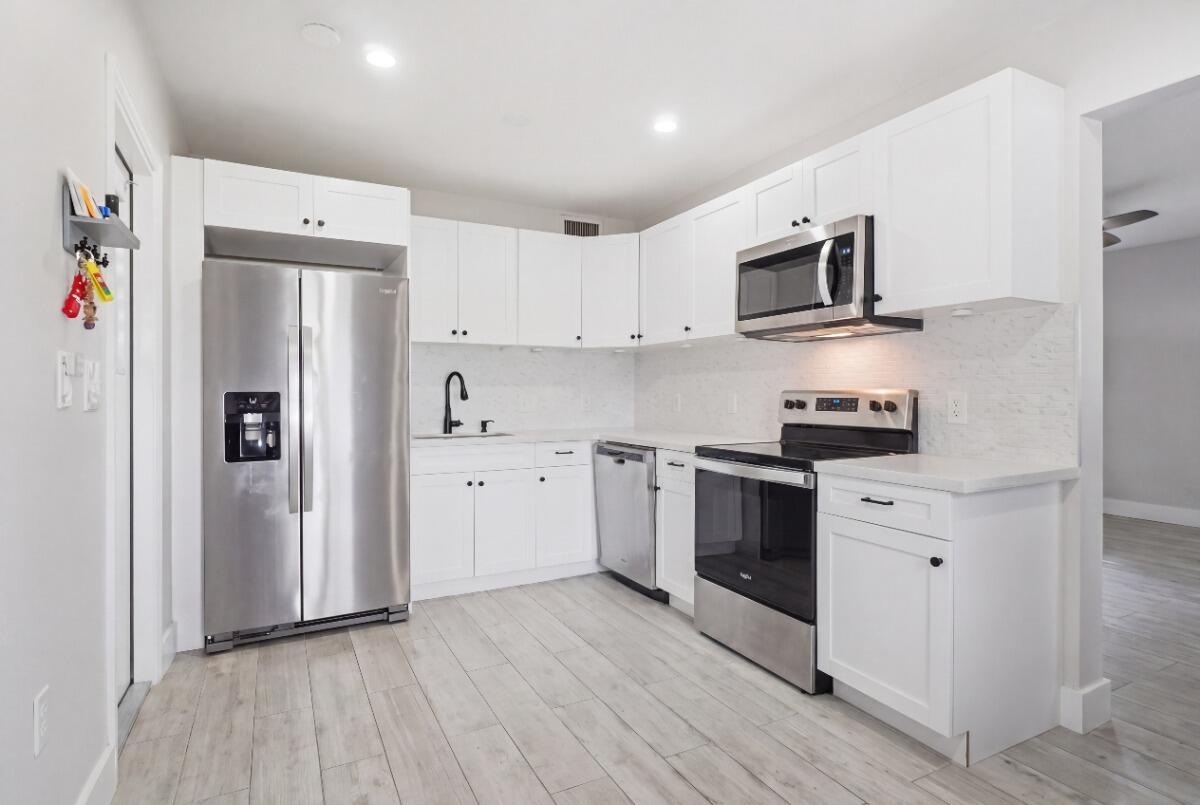 A kitchen with white cabinets, stainless steel appliances, and light wood-look flooring — 712 NE 10th Avenue, Pompano Beach FL 33060, POMPANO BEACH, FL