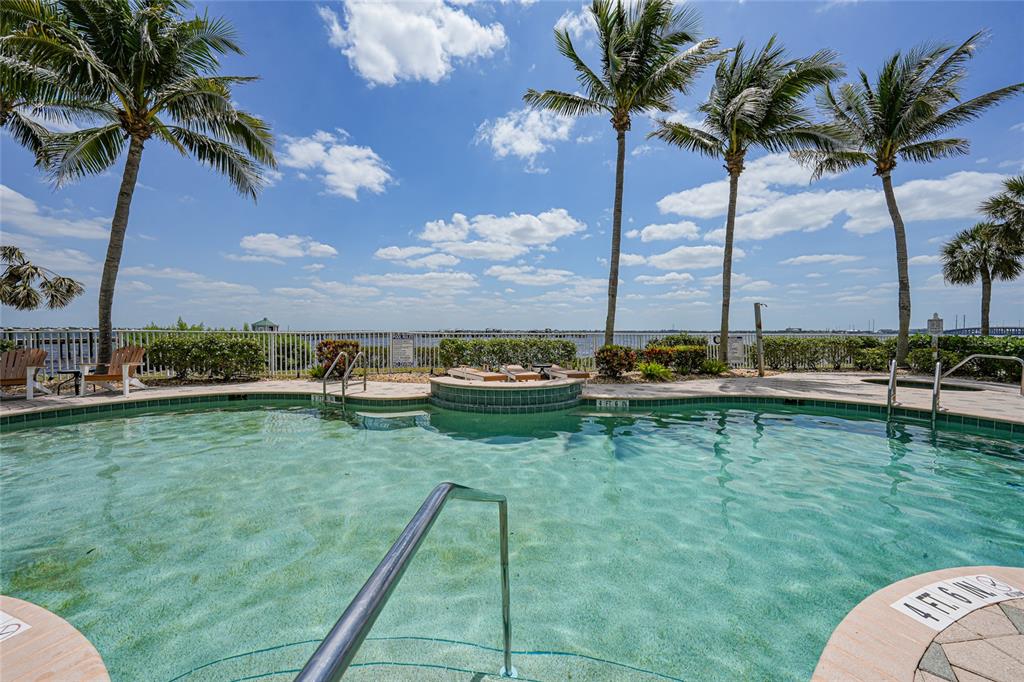 A swimming pool with a metal handrail overlooks a waterfront view with palm trees — 5114 MELBOURNE STREET UNIT A202, PUNTA GORDA, FL