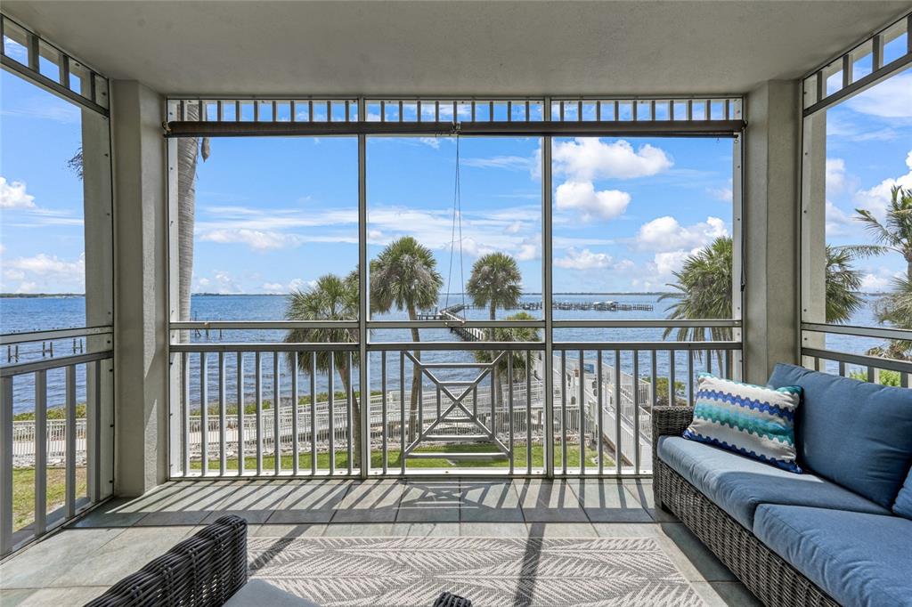 A screened-in porch features wicker furniture and a view of a pier and water — 5114 MELBOURNE STREET UNIT A202, PUNTA GORDA, FL