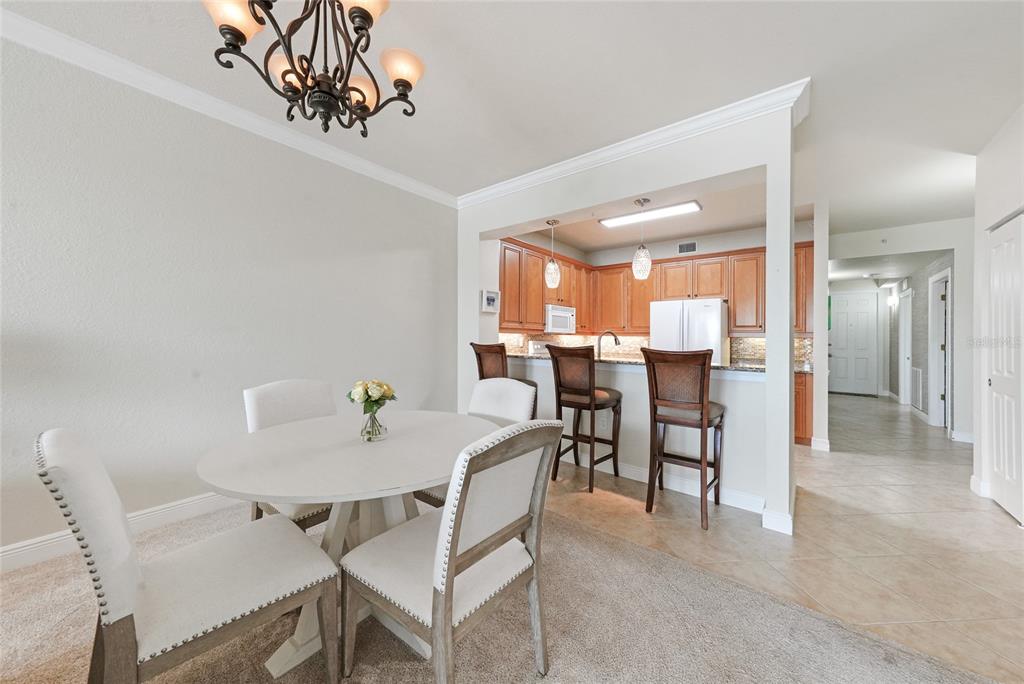 A dining area with a round table and chairs sits adjacent to a kitchen with barstools — 5114 MELBOURNE STREET UNIT A202, PUNTA GORDA, FL