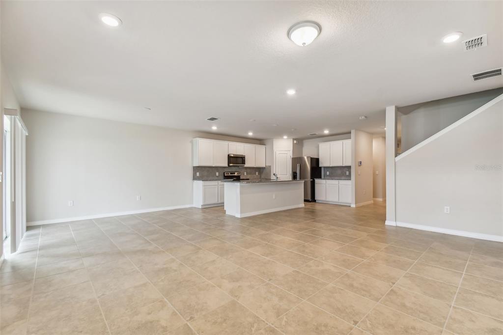 An open-concept kitchen with white cabinets and a center island overlooks a tiled living area — 33323 HERDS HALLOW WAY, WESLEY CHAPEL, FL