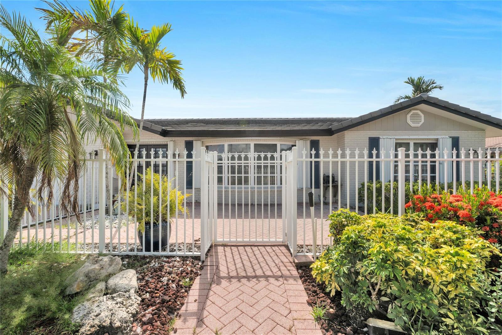 A single-story house with a white metal fence, brick walkway, and palm trees in front — 4020 NE 24th Avenue, Lighthouse Point FL 33064, LIGHTHOUSE POINT, FL