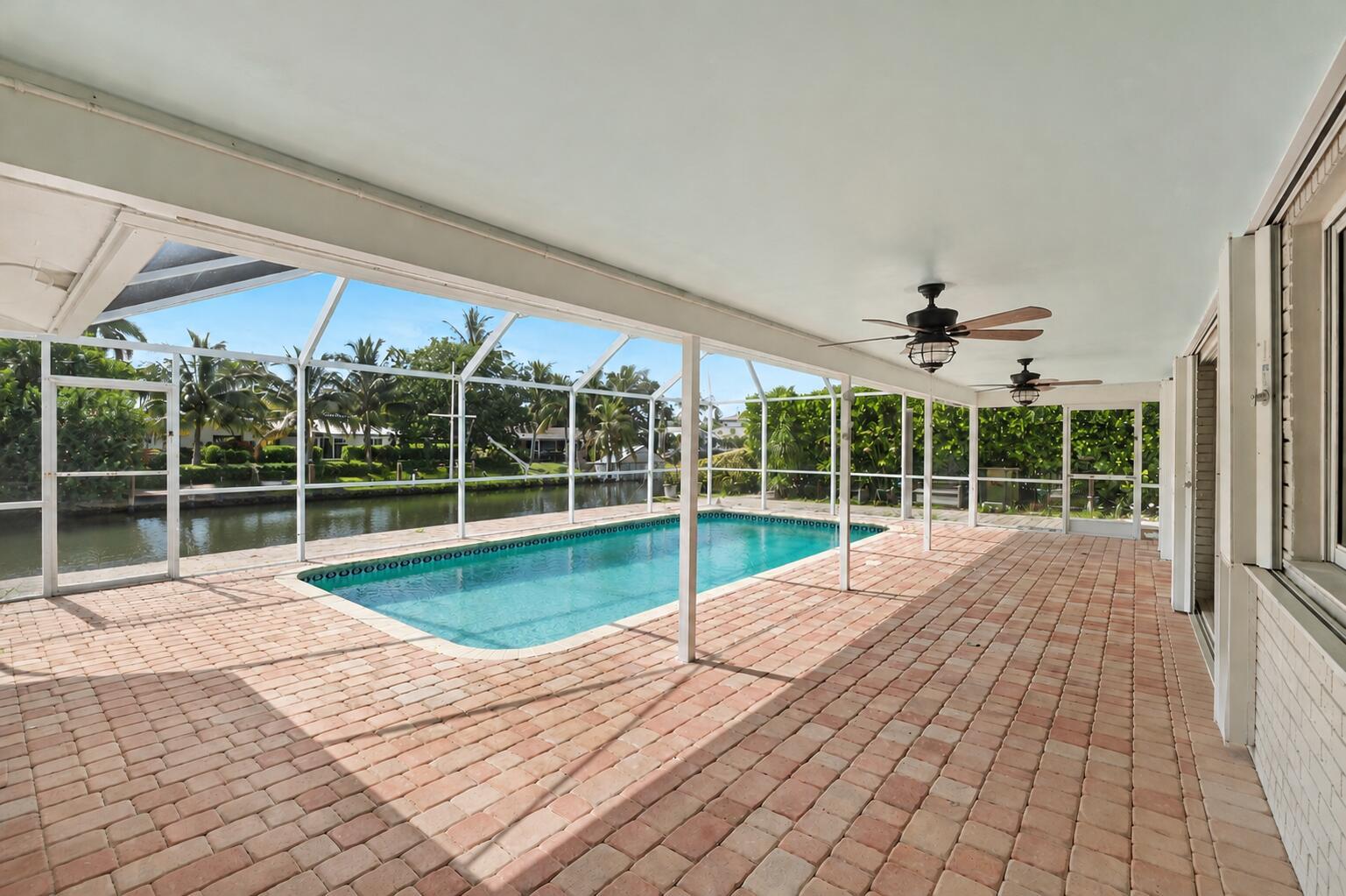 A covered brick patio features a screened-in swimming pool overlooking a canal and palm trees — 4020 NE 24th Avenue, Lighthouse Point FL 33064, LIGHTHOUSE POINT, FL