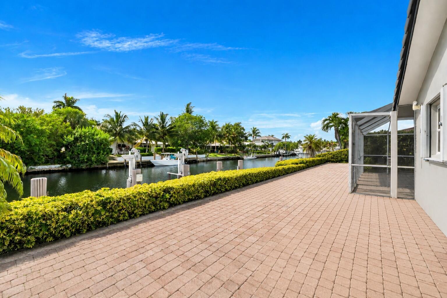 A paved patio overlooks a canal with a boat dock and lush tropical landscaping — 4020 NE 24th Avenue, Lighthouse Point FL 33064, LIGHTHOUSE POINT, FL